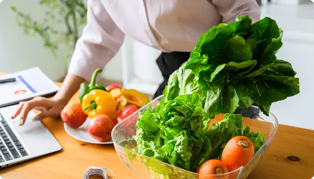 野菜とパソコンが置かれた作業風景の写真