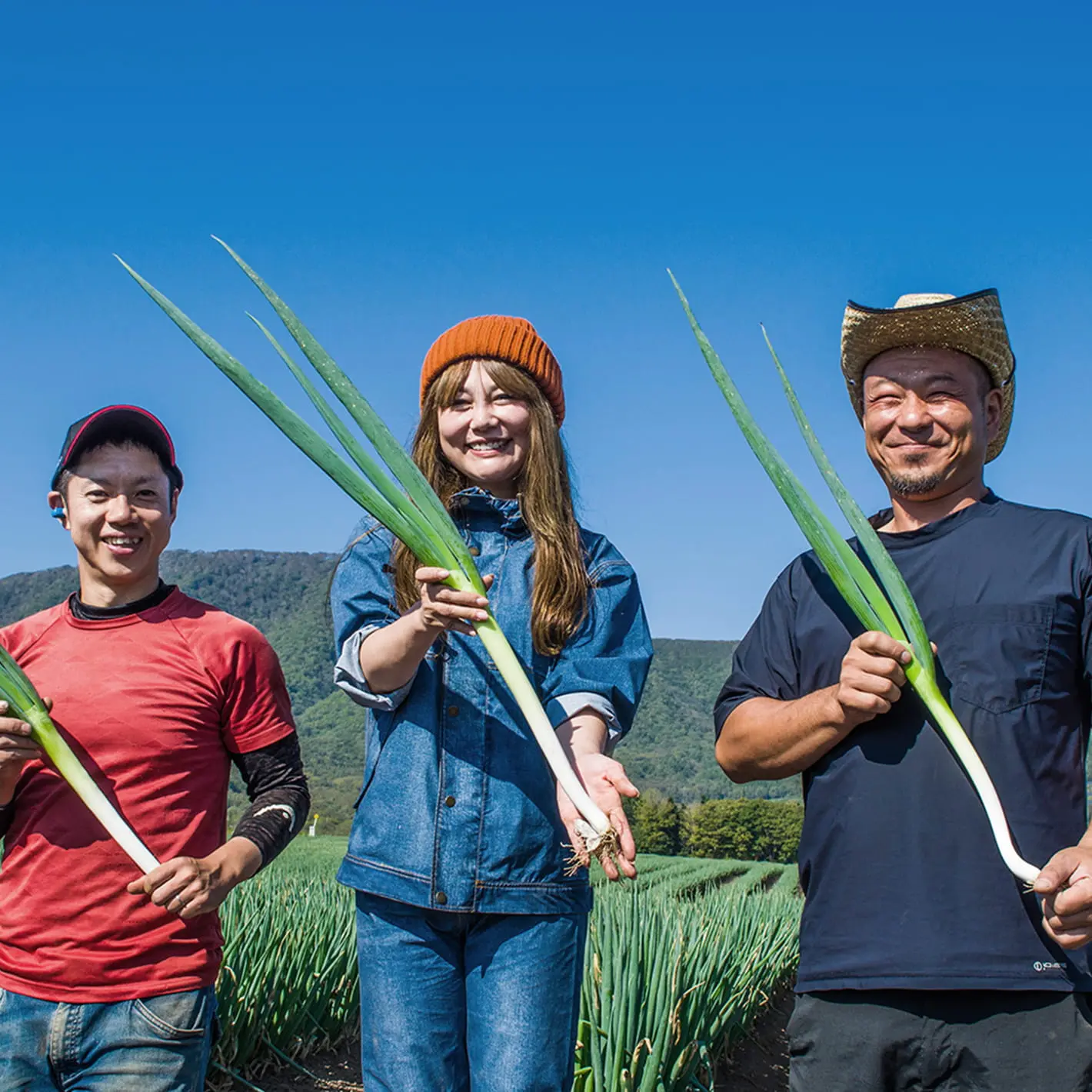 畑で収穫した長ねぎを手に笑顔で並ぶ生産者たち